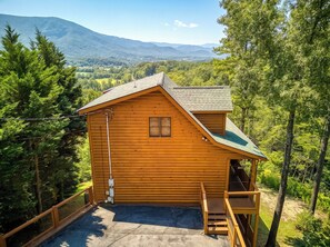 Eine Holzhütte mit einem Balkon, umgeben von Bäumen und einer Berglandschaft.