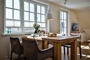 A modern kitchen with a wooden table, four chairs, a hanging light fixture, and large windows. - Experience the ultimate vacation at Haus am Meer Strandburg on Sylt (Wenningstedt-Braderup (Sylt))