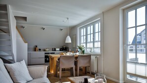 Een moderne woonkamer met een bank, een eettafel met stoelen, en een keuken op de achtergrond.