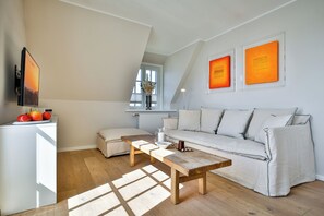 A modern living room with a wooden bench, a white sofa, and a flat-screen TV mounted on the wall. - Experience the ultimate vacation at Haus am Meer Strandburg on Sylt (Wenningstedt-Braderup (Sylt))