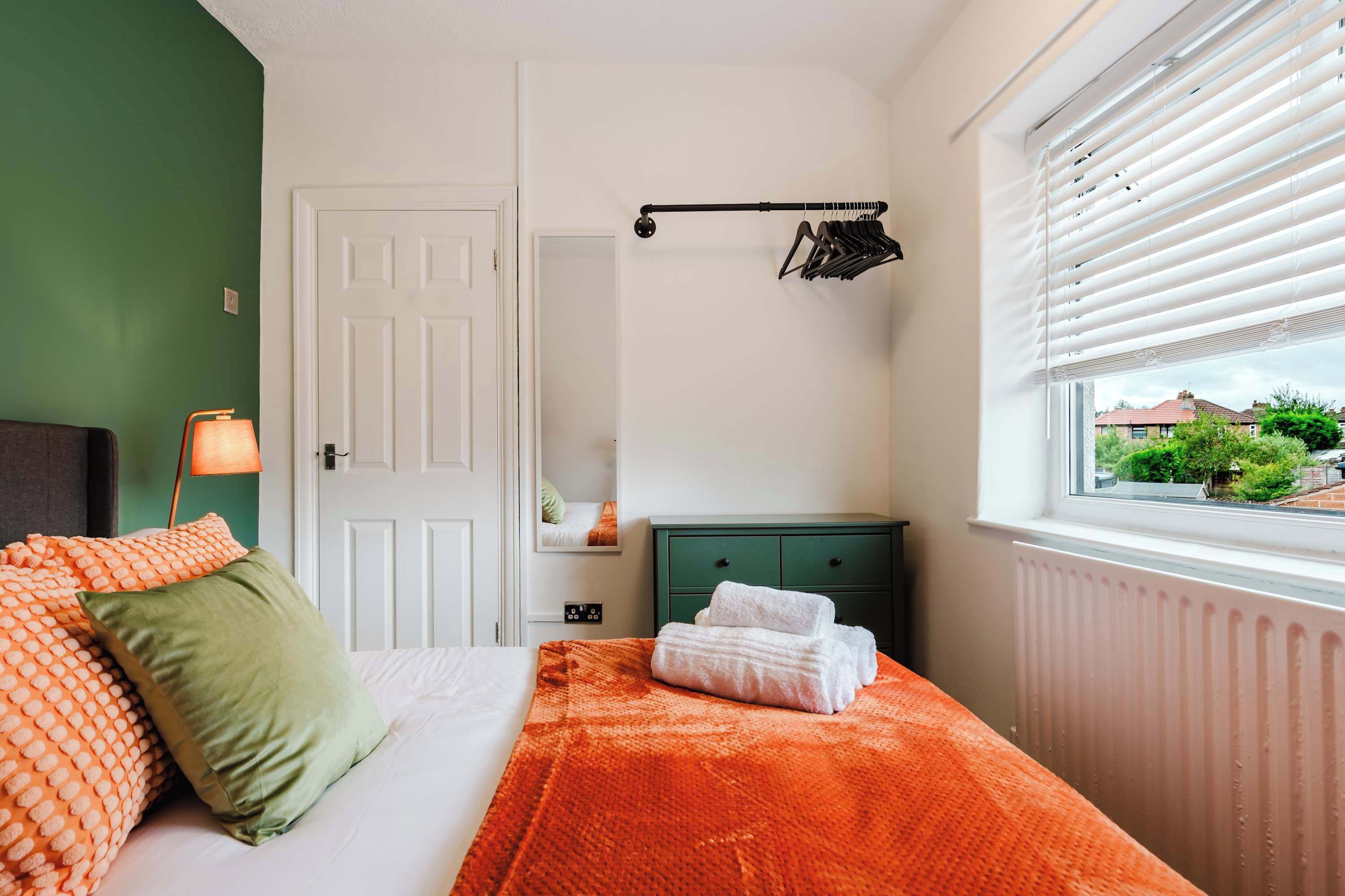 A bedroom with a bed, a window with blinds, a radiator, and a green dresser.