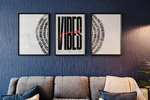 Drei gerahmte Kunstwerke mit Blättermotiv an einer blauen Wand mit Struktur, ein graues Sofa mit Kissen und eine Topfpflanze.