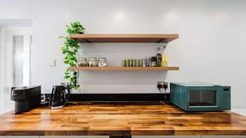 A kitchen with a wooden countertop, a coffee maker, a microwave, and shelves with jars and a plant.