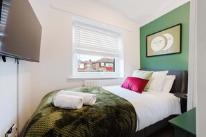 Ein Hotelzimmer mit Bett, einem Fenster mit Jalousien, einem gerahmten Bild an der Wand und einem Fernseher.