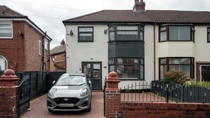 A residential property with a car parked in the driveway, a gated entrance, and a two-story house with a bay window. - Etihad & Co-op Live, 3-Bed, Free Parking (Droylsden)