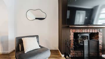 Ein Wohnzimmer mit grauem Sofa, einem flachbildfernseher über einem Kamin aus Ziegelsteinen und einem an der Wand befestigten Spiegel.