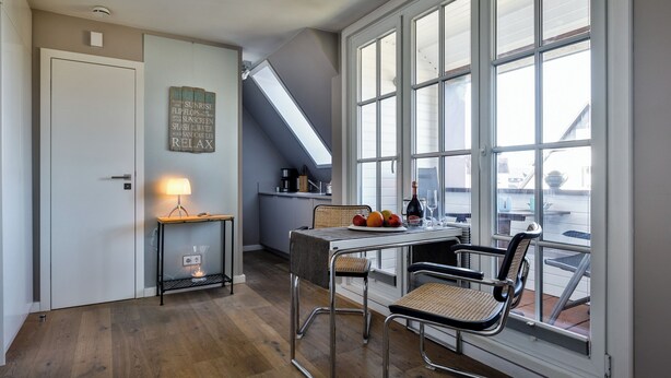 Ein Zimmer mit Esstisch, Stühlen, einer Lampe und einem großen Fenster mit vielen Fensterscheiben.