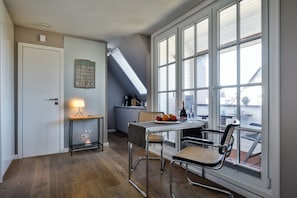 Ein Zimmer mit Esstisch, Stühlen, einer Lampe und einem großen Fenster mit vielen Fensterscheiben.