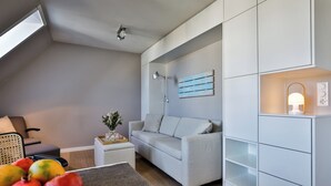 Ein modernes Wohnzimmer mit einem grauen Sofa, einem kleinen Beistelltisch, einer Wandregal und einer Deckenleuchte.