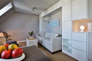 Ein modernes Wohnzimmer mit einem grauen Sofa, einem kleinen Beistelltisch, einer Wandregal und einer Deckenleuchte.