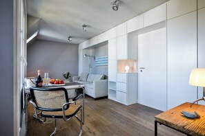 Eine moderne Küche mit weißen Schränken, eine Essecke mit einem Korbstuhl und einem Holztisch mit Flasche und Gläsern.