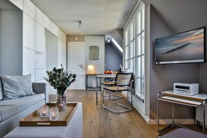 Un salon moderne comprenant un canapé, une table basse agrémentée d’objets décoratifs, un coin repas avec une table et des chaises, un téléviseur à écran plat fixé au mur et une petite kitchenette équipée d’un grille-pain.