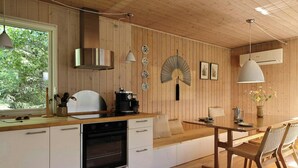 A modern kitchen with wooden walls, a built-in oven, a dining area with a table and chairs, and a large window providing natural light. - Holiday home with terraces near Udsholt Strand (Udsholt)