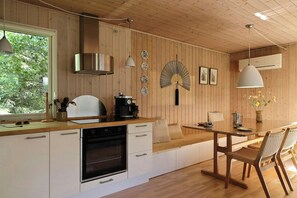 Eine moderne Küche mit Holzwänden, einem eingebauten Ofen, einer Essecke mit Tisch und Stühlen sowie einem großen Fenster, das natürliches Licht hereinlässt.