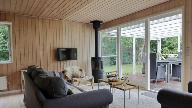 A modern living room with a sofa, a television, a fireplace, and a view of the outdoors. - Holiday home with terraces near Udsholt Strand (Udsholt)