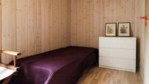 A bedroom with a wooden wall, a bed with a purple bedspread, a white dresser, and two framed pictures on the wall. - Holiday home with terraces near Udsholt Strand (Udsholt)