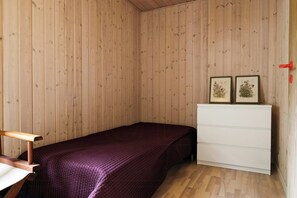 Ein Schlafzimmer mit einer Holzwand, einem Bett mit violettem Überwurf, einer weißen Kommode und zwei gerahmten Bildern an der Wand.