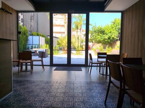 A modern interior with a patterned floor, wooden furniture, and large glass doors leading to an outdoor area with greenery and a building in the background. - HOTEL PIETRA NERA (Catania)