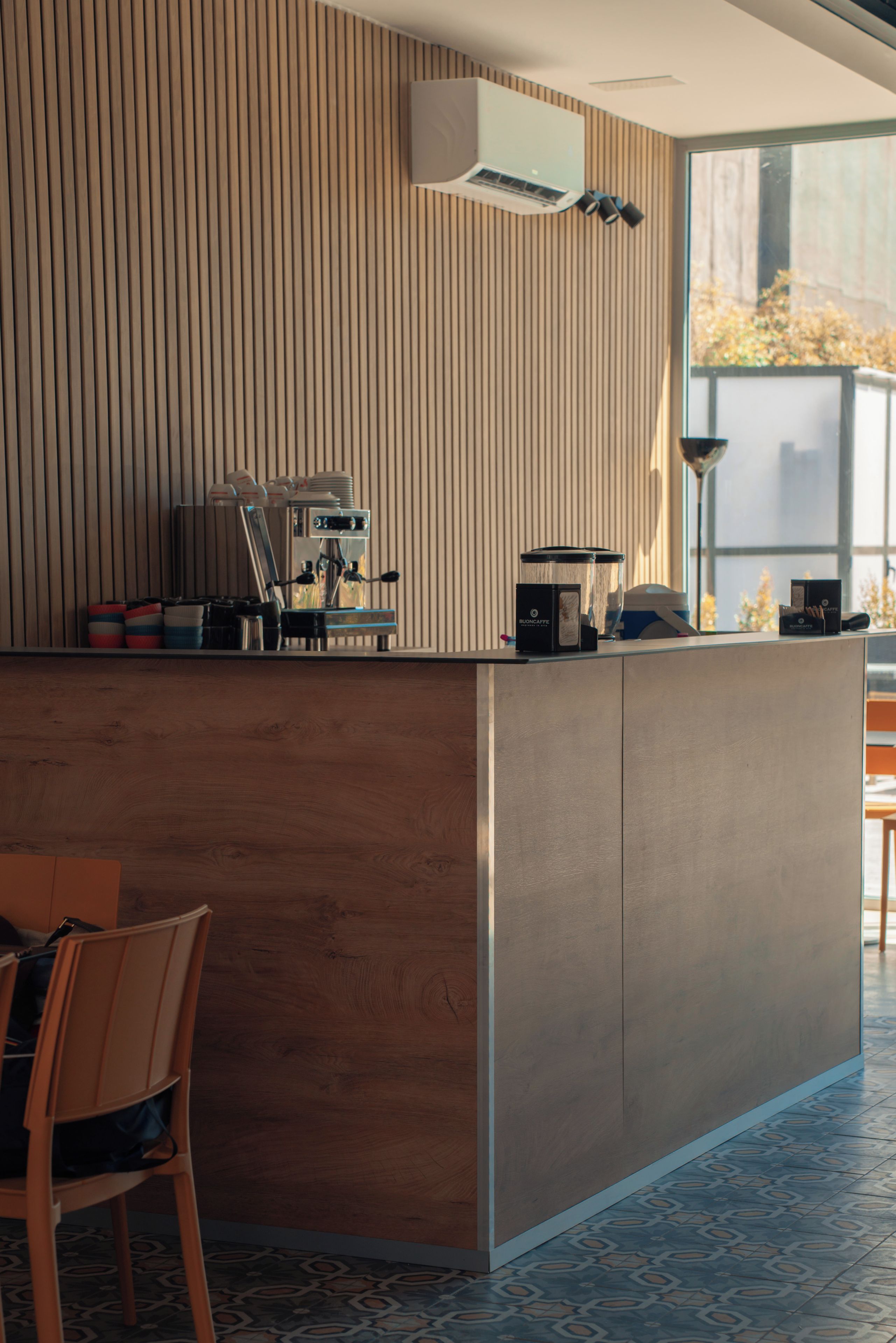 Um balcão de recepção moderno com uma máquina de café, um recipiente de vidro e uma pequena caixa com a inscrição 'BUONCAFÉ'.