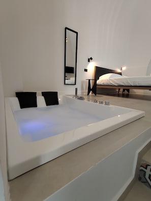 Un baño moderno con una bañera grande, un espejo y una cama al fondo.