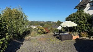 Ein Pflasterweg führt zu einer Terrasse mit Gartenmöbeln und einem weißen Sonnenschirm.