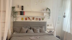 A neatly made bed with a grey headboard, a bedside table with a lamp, and a wall decorated with circular ornaments and a string of lights. - Studio Jardin Harmonie, sehr elegant wohnen Pantry-Küche, Terrasse, Garten, Pool (Rain)