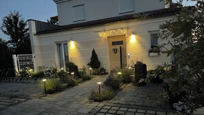 A residential building with a paved driveway, a gated entrance, and outdoor lighting. - Studio Jardin Harmonie, sehr elegant wohnen Pantry-Küche, Terrasse, Garten, Pool (Rain)