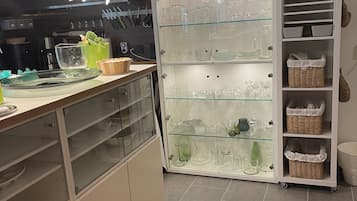 A modern kitchen with a glass display cabinet filled with glassware and a white cabinet with storage baskets.
