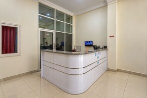 A reception area with a curved counter, a television screen, and a window with a red curtain. - Hotel O Wisma Fortuner (Makassar)