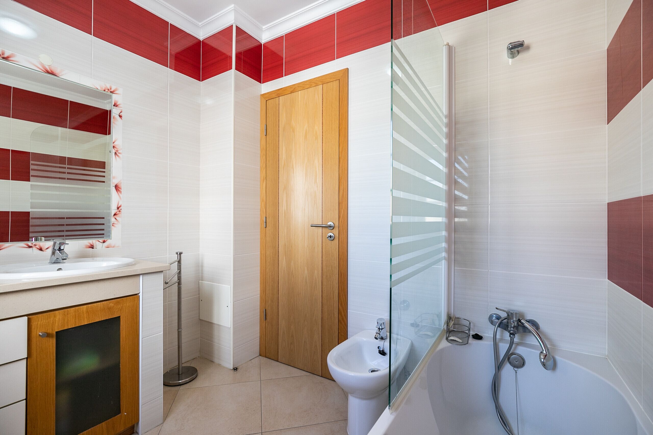 Un baño con puerta de madera, cabina de ducha de vidrio, lavabo con espejo y un bidé.