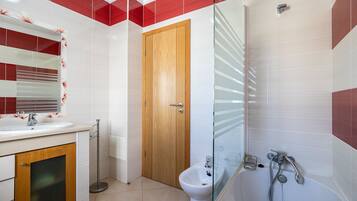Un baño con puerta de madera, cabina de ducha de vidrio, lavabo con espejo y un bidé.