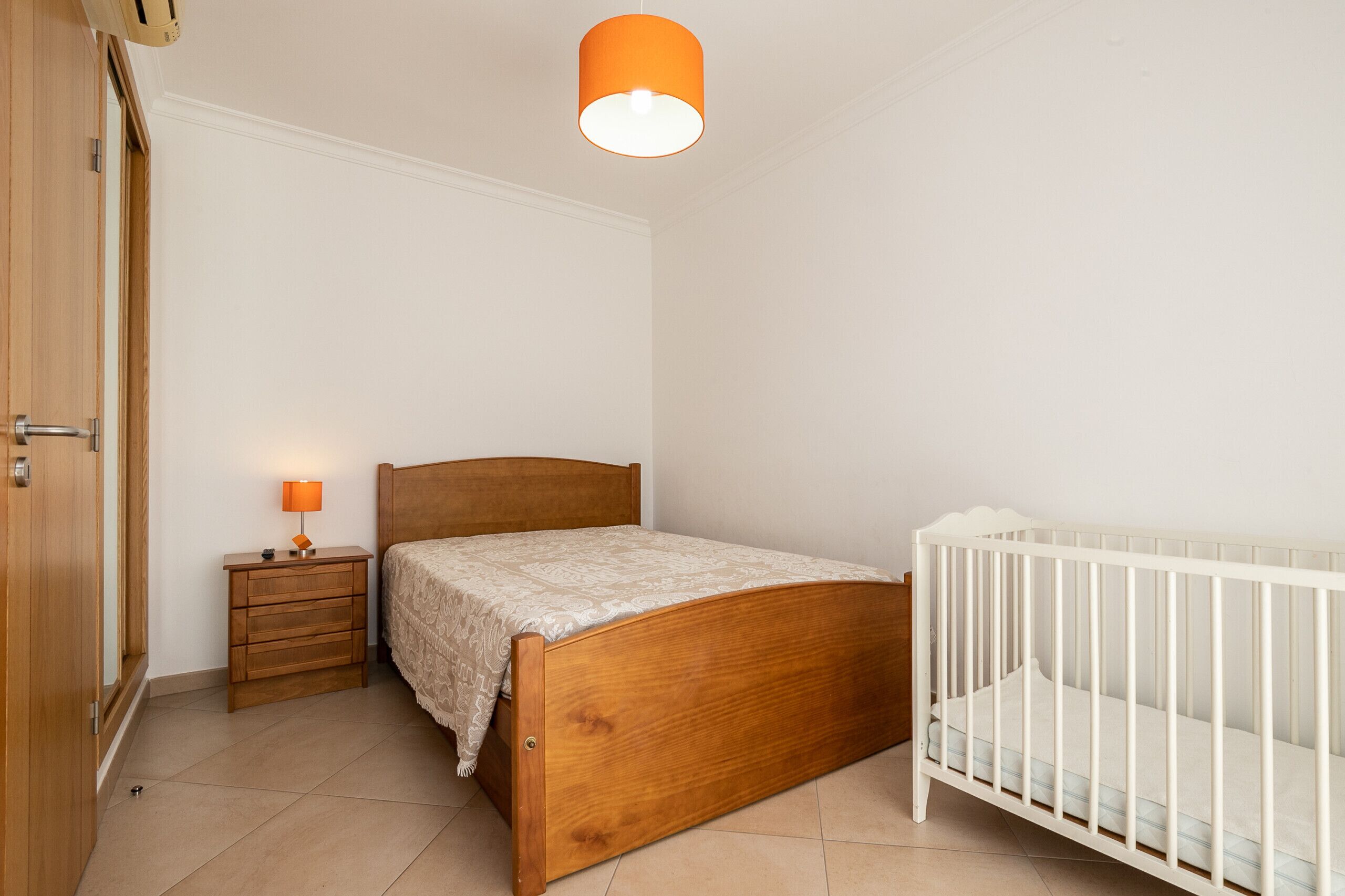 Une chambre à coucher avec un lit en bois, une table de chevet avec une lampe, un berceau blanc et une porte.