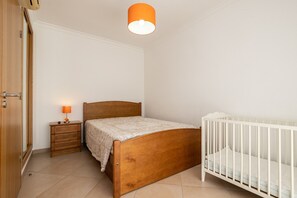 Una camera da letto con un letto di legno, un comodino con una lampada, una culla bianca e una porta.