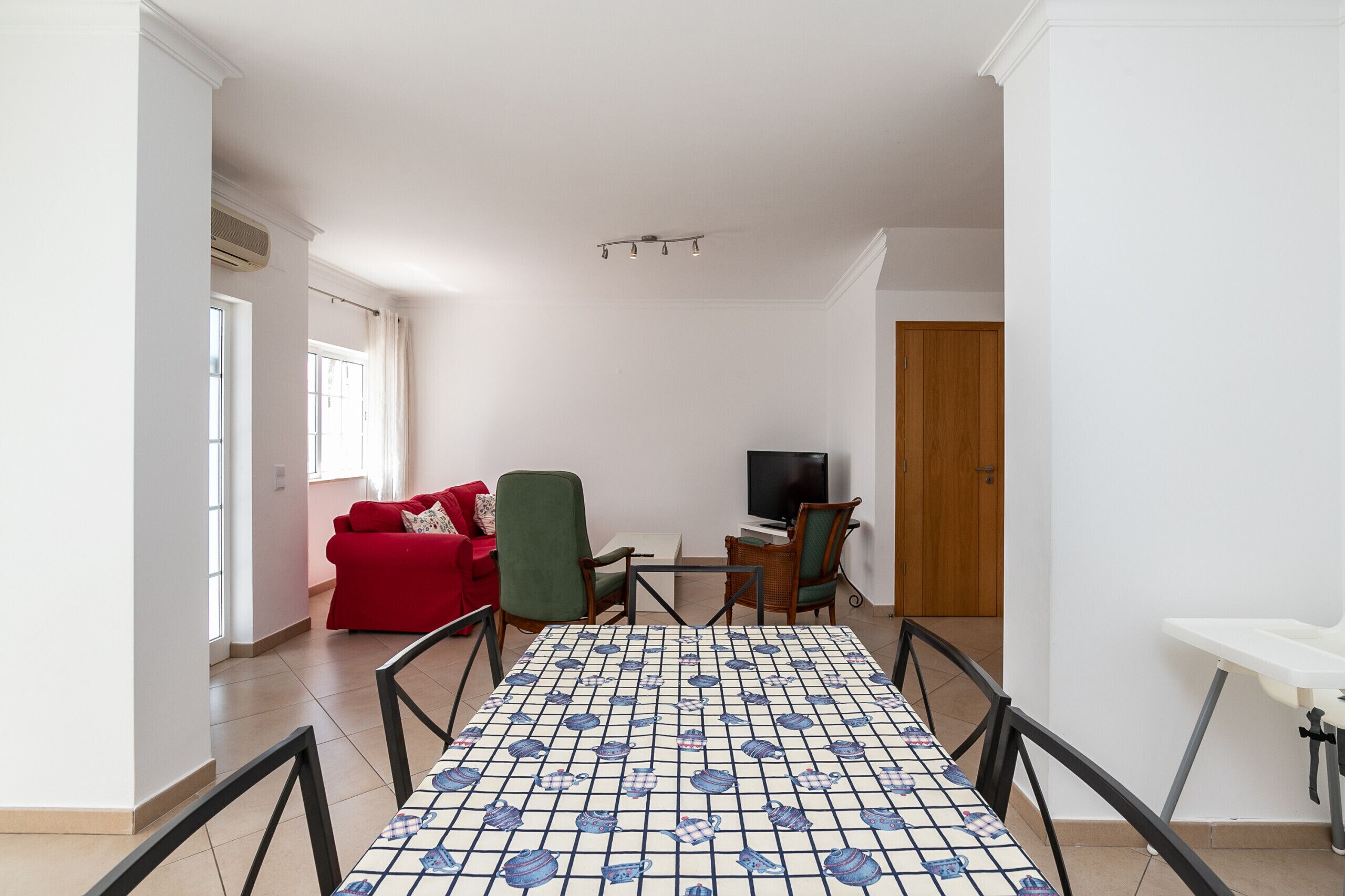 Un salon avec un canapé rouge, un fauteuil vert, un téléviseur et une table à motifs.