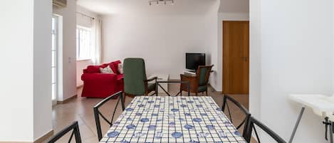 Ein Wohnzimmer mit einem roten Sofa, einem grünen Sessel, einem Fernseher und einem Tisch mit Muster.