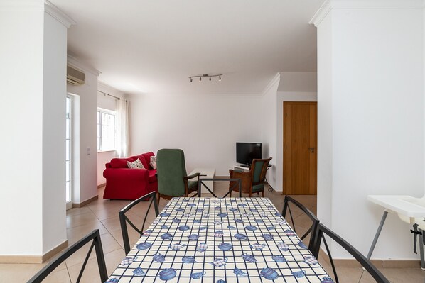 A living room with a red sofa, a green armchair, a television, and a patterned table.