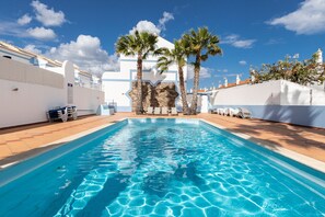 A swimming pool with clear blue water, surrounded by white walls and palm trees.