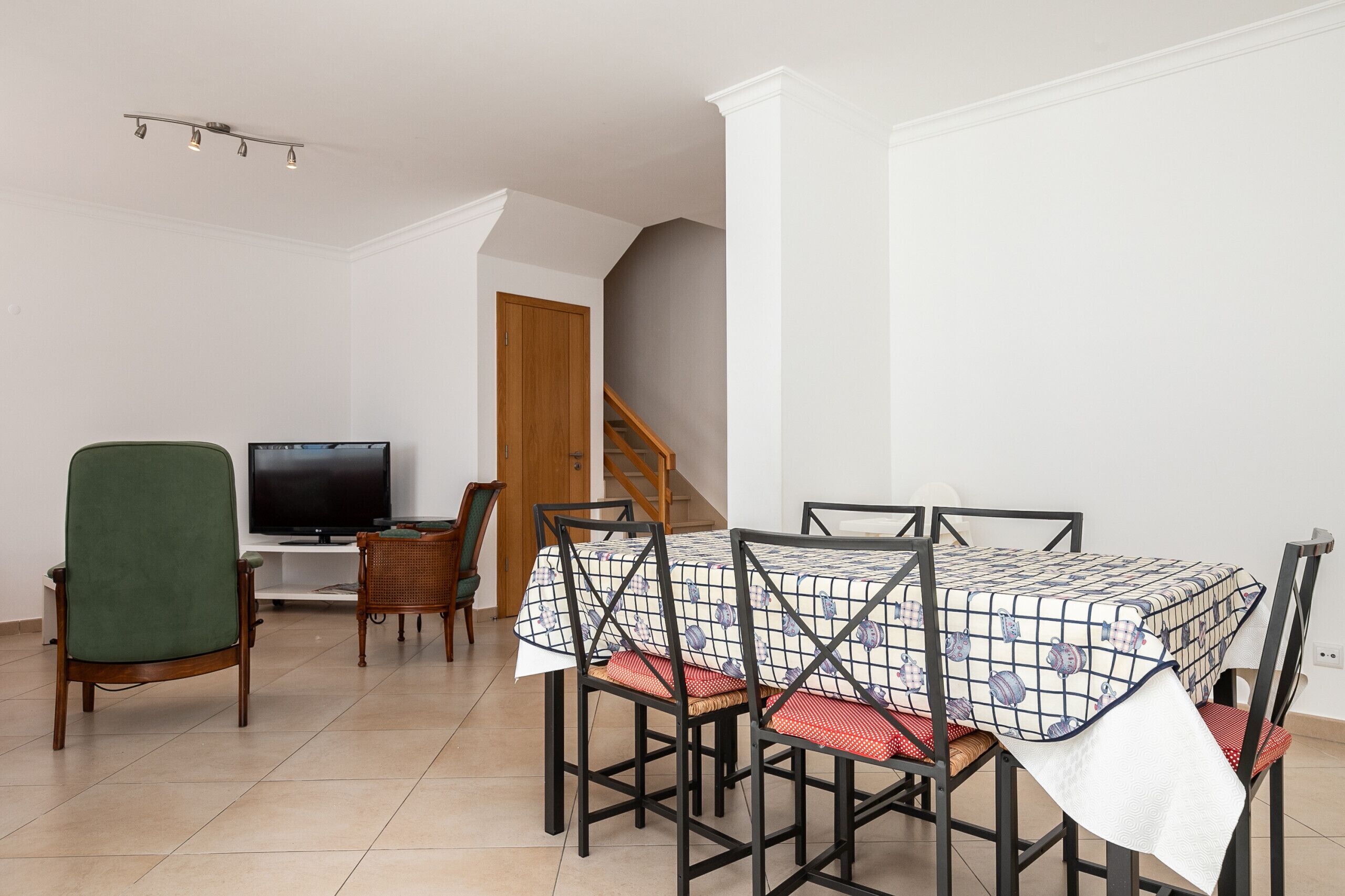 Un comedor con una mesa dispuesta para cuatro, un televisor y una escalera que sube a un nivel superior.