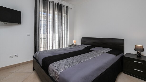 A modern bedroom with a bed, a nightstand, a lamp, and a TV mounted on the wall.