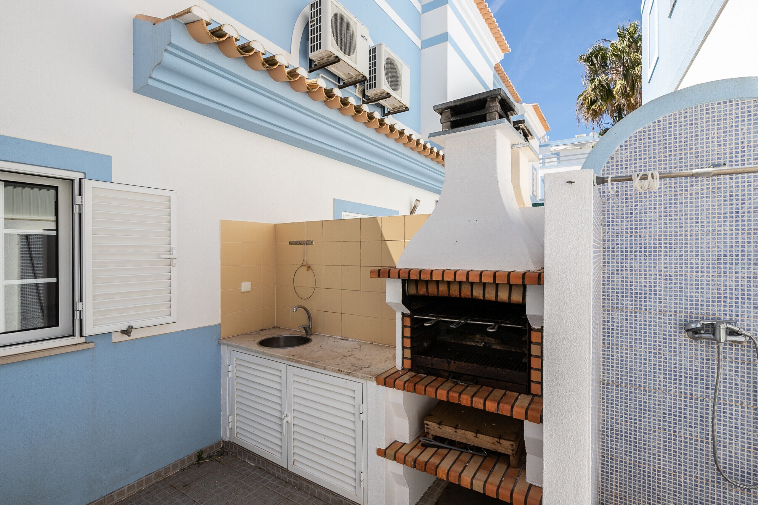 A compact kitchen with a built-in grill, a window with shutters, and a tiled backsplash.