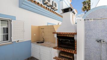 A compact kitchen with a built-in grill, a window with shutters, and a tiled backsplash.