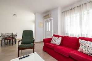 A living room with a red sofa, a green armchair, a dining table with chairs, and a white coffee table.