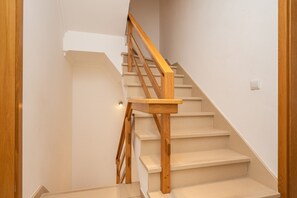 A wooden staircase with a handrail, leading to a landing with a light switch.