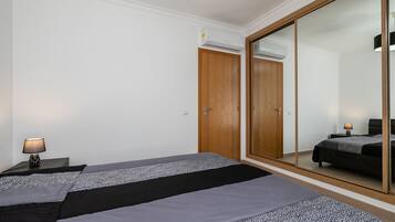 A bedroom with a bed, a nightstand, a lamp, a wardrobe, and a large mirror.