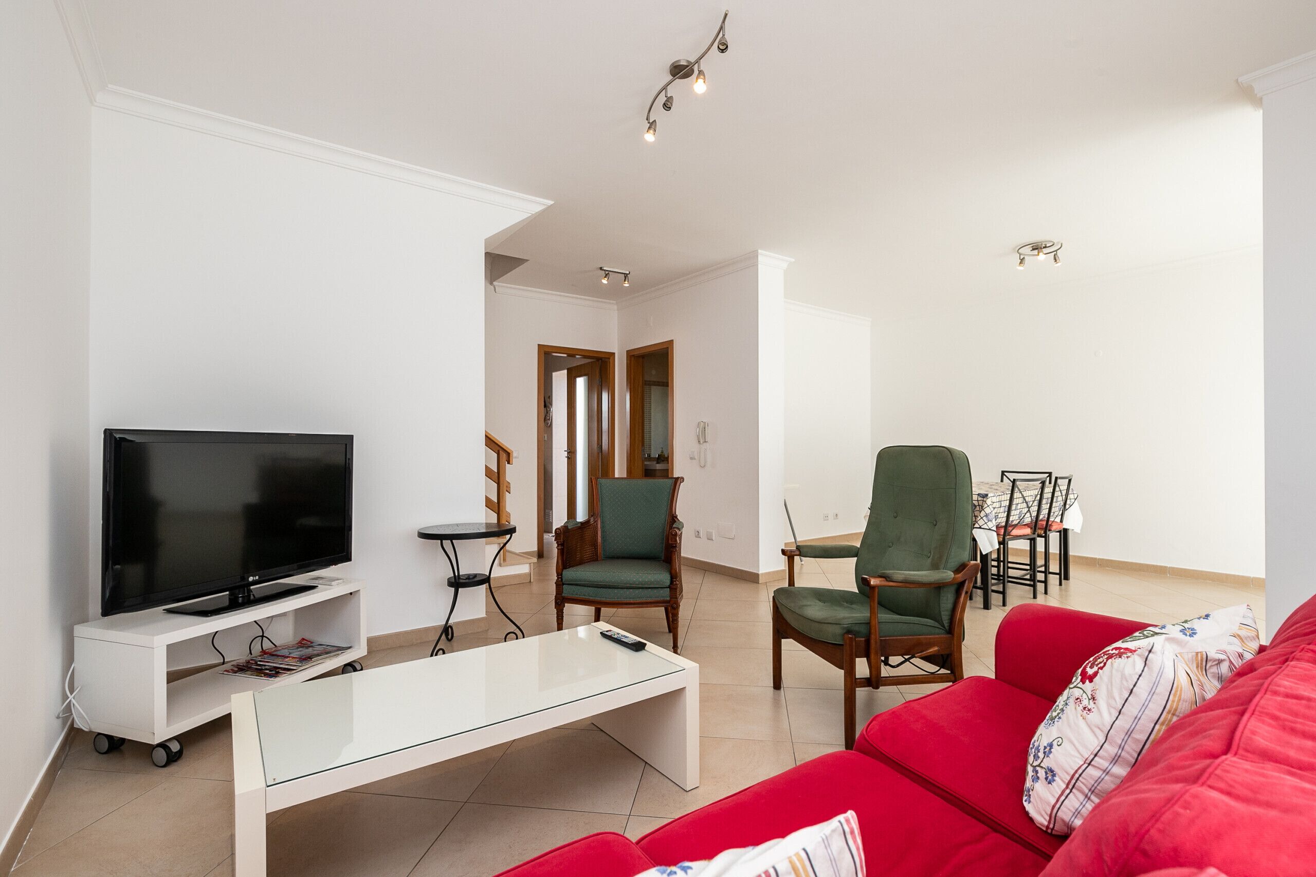 En stue med et fladskærms-tv, et glasbord, en rød sofa og et spiseområde med stole og et bord.