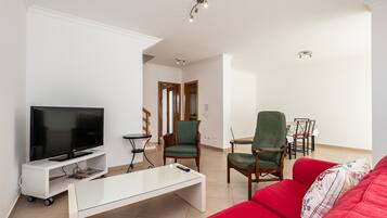 A living room with a flat-screen TV, a glass coffee table, a red sofa, and a dining area with chairs and a table.