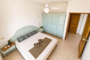 Ein Schlafzimmer mit Bett, Nachttisch, Kleiderschrank und Deckenventilator.