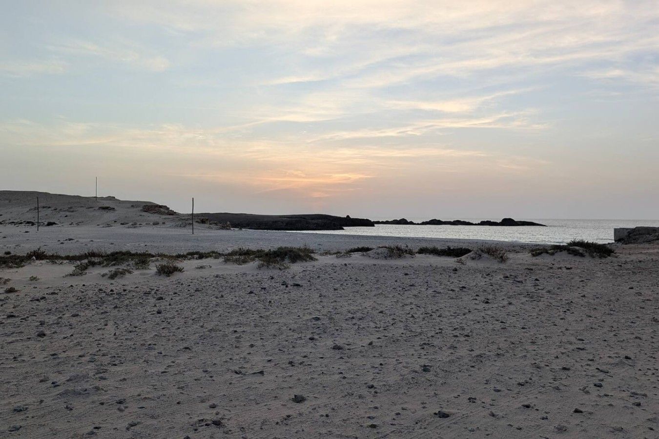Een strand met duinen en een rustige zee onder een heldere lucht.