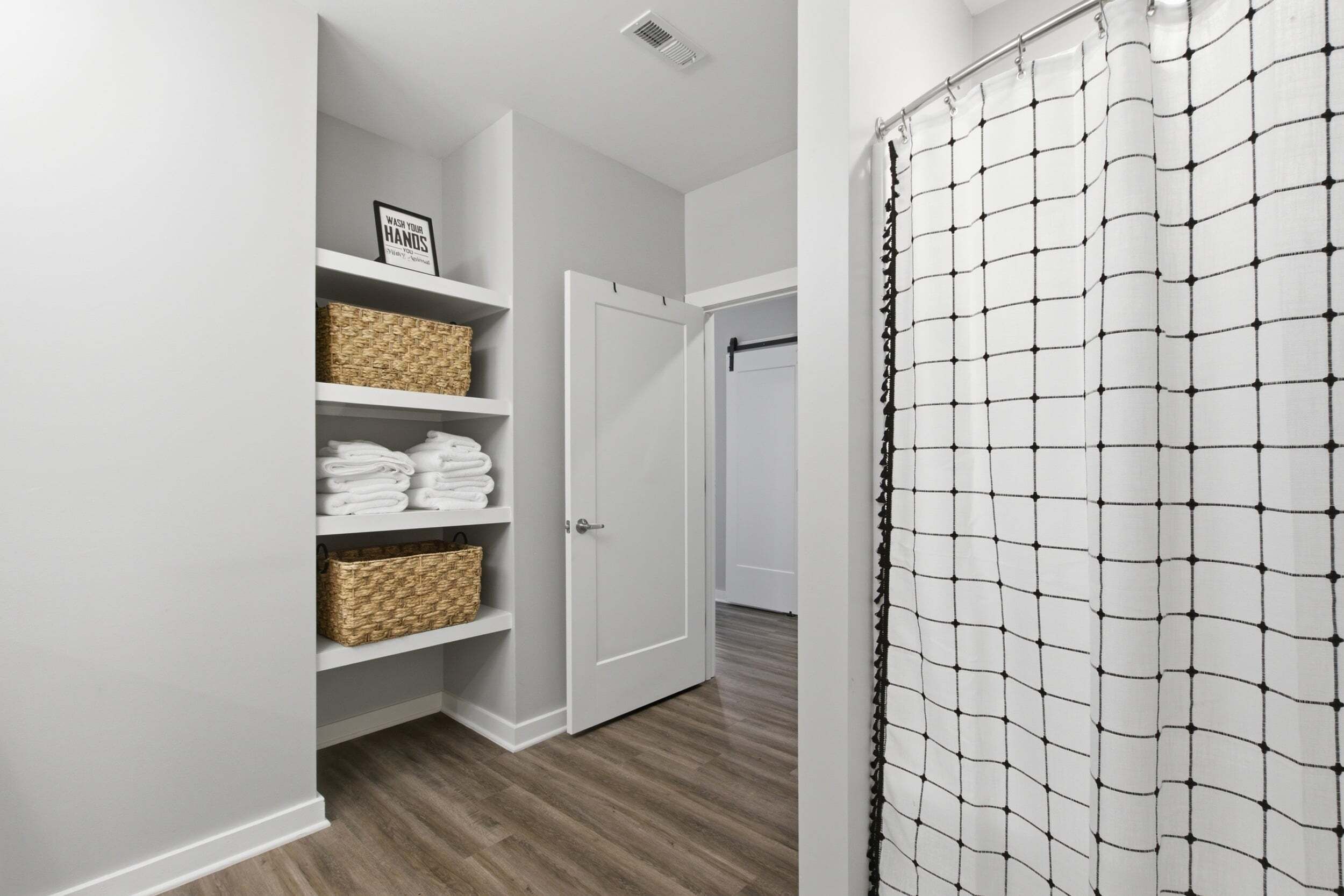 A bathroom with a shower curtain, a white door, and a shelf with towels and baskets.