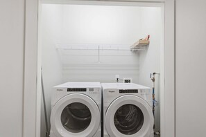 A laundry room with two front-loading Whirlpool washers and a metal shelf above them. - The Prince Penthouse - Walkable & Free Parking! (Athens)